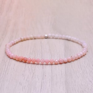 May include: A delicate pink opal gemstone bracelet with a silver clasp. The bracelet is made of small, round beads that are strung together on a thin cord.