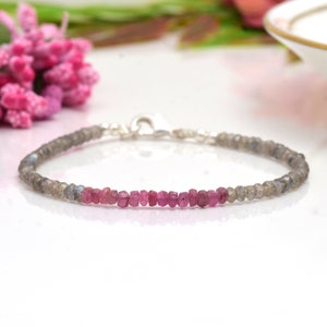May include: A delicate bracelet made with small, faceted pink and gray gemstones. The bracelet has a silver clasp.