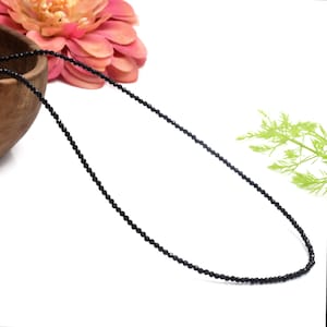 Op de afbeelding: Een zwarte kralenketting gemaakt van kleine, gefacetteerde zwarte onyx kralen. De ketting is geregen op een dun, zwart koord en is ongeveer 45 cm lang.