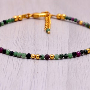 May include: A delicate gold chain bracelet with green, black, and purple gemstone beads.