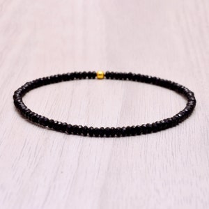 Pode incluir: Um bracelete preto de contas com um acento de contas douradas.