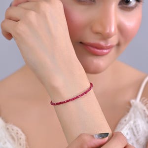 May include: A fine bracelet composed of small, vivid red beads. The bracelet is displayed on a wrist, highlighting its simple and elegant design. The beads are evenly sized and closely spaced, forming a continuous line of colour. The bracelet is approximately 17 cm in length.
