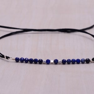 May include: A delicate blue and silver beaded bracelet with a black cord and silver clasp.