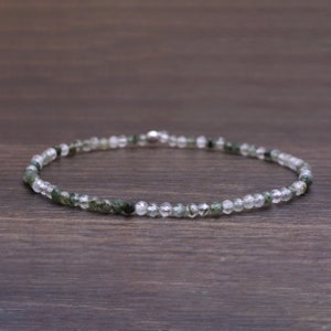 May include: A delicate necklace made with small, clear and green gemstone beads. The necklace is strung on a silver chain.