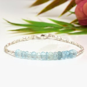 May include: A delicate silver bracelet with a row of light blue aquamarine beads. The bracelet has a silver clasp.