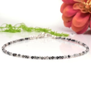 以下が含まれることがあります： 小さく丸い黒と白の宝石ビーズがついた、繊細な銀のチェーンブレスレットです。