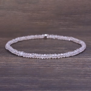 May include: A delicate necklace made of small, clear, faceted beads. The necklace is on a wooden surface.
