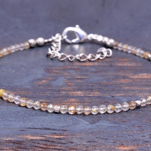 以下が含まれることがあります： 小さなクリアクォーツビーズが施された、繊細なシルバーチェーンブレスレット。ビーズは、かすかに金色に輝いています。ブレスレットは、ロブスタークラスプで留められています。