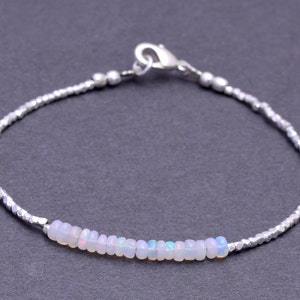 May include: A delicate silver chain bracelet with a row of white opal beads. The bracelet has a silver clasp.