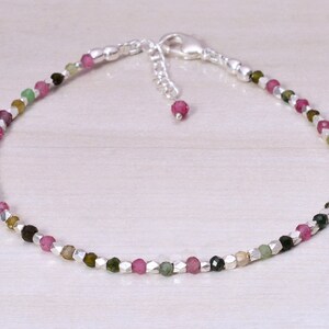 May include: A delicate silver anklet with a chain closure and a mix of small, faceted gemstones in shades of pink, green, and black.