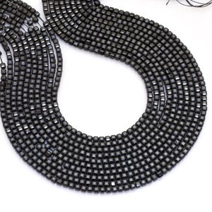 May include: Close-up of multiple strands of small, square, dark grey beads. The beads are strung together, creating a textured surface. The beads are uniform in size and shape, and the overall effect is sleek and modern.