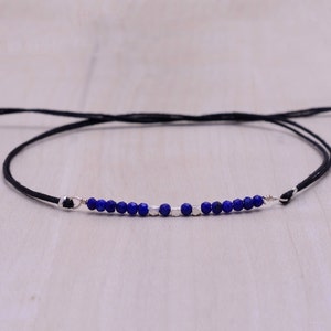May include: A simple black cord bracelet with a row of small blue lapis lazuli beads and silver spacer beads.