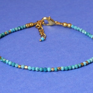May include: A turquoise and gold beaded anklet with a gold clasp.