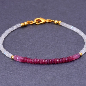 Puede incluir: Un brazalete delicado con una fila de cuentas de rubí rosa y una fila de cuentas de piedra lunar blanca. El brazalete tiene un cierre dorado.