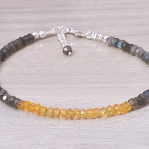 Puede incluir: Un delicado brazalete de cadena de plata con una mezcla de cuentas de labradorita gris oscuro y citrino amarillo.