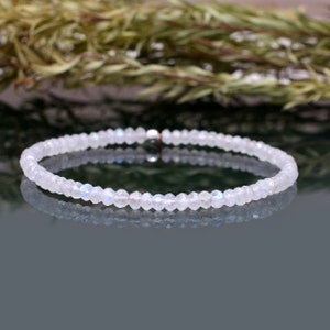 Könnte beinhalten: Ein zartes Armband aus weißem Mondstein mit einem silbernen Verschluss. Das Armband besteht aus kleinen, runden Perlen und hat einen dezenten, schimmernden Effekt.