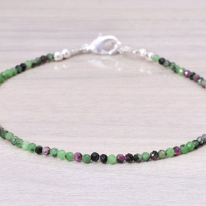 Puede incluir: Un delicado brazalete de piedras preciosas verdes, negras y rosas con un cierre plateado.