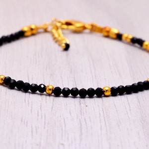 Könnte beinhalten: Ein zartes Armband aus schwarzen und goldenen Perlen mit einem Verschluss. Das Armband besteht aus kleinen, facettierten schwarzen Perlen und goldenen Akzentperlen.