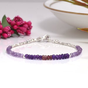 May include: A delicate silver chain bracelet with a gradient of amethyst and pink gemstone beads. The bracelet features a silver clasp.