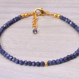 Peut inclure: Un bracelet délicat en saphir bleu avec des accents dorés. Le bracelet est doté d'une fermeture à fermoir et d'un petit charme en or.