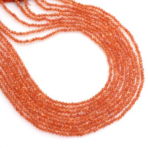 Puede incluir: Múltiples hilos de cuentas facetadas de piedra solar naranja. Las pequeñas cuentas uniformes tienen una calidad brillante y reflectante. Los hilos caen en cascada, creando una sensación de abundancia y textura. Las cuentas son de un color cálido y terroso.