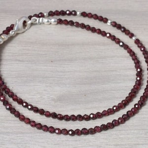 Könnte beinhalten: Eine doppelreihige Halskette aus kleinen, dunkelroten Granatperlen mit einem silbernen Verschluss.