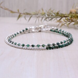 May include: A delicate double strand bracelet featuring green emerald beads and silver beads.