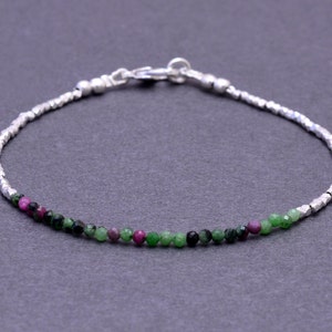 Puede incluir: Un brazalete de cadena de plata con piedras preciosas verdes y rosas. El brazalete tiene un cierre de langosta.