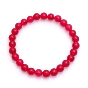 May include: A vibrant red beaded bracelet. The bracelet is composed of numerous round, polished beads. The beads are a deep, saturated red color, and are strung together to form a circular shape. The bracelet is displayed against a white background.