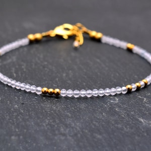 Puede incluir: Un brazalete delicado con cuentas de cuarzo transparente y detalles dorados. El brazalete está hecho con cuentas pequeñas y redondas y tiene un diseño simple y elegante.