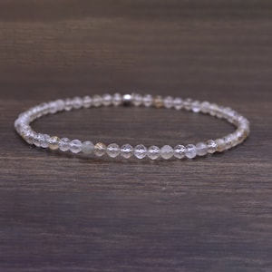 Könnte beinhalten: Ein zartes Armband aus klaren Quarzperlen mit einem dezenten goldenen Schimmer. Die Perlen sind facettiert und haben eine leicht unregelmäßige Form, was dem Armband einen einzigartigen und natürlichen Look verleiht.