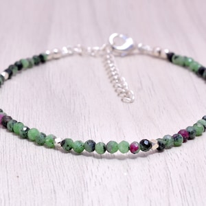 Könnte beinhalten: Ein zartes Armband aus grünen, schwarzen und rosafarbenen Edelsteinperlen mit silbernen Akzenten.