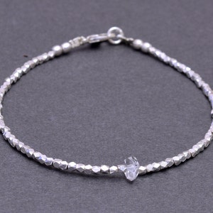 May include: A silver bracelet with a faceted crystal charm. The bracelet is made of small, silver beads.