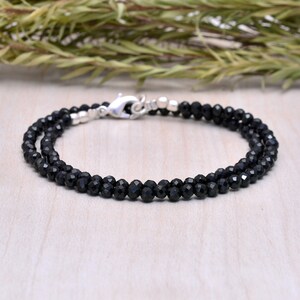 Könnte beinhalten: Ein Armband aus schwarzen Edelsteinen mit einem silbernen Verschluss. Das Armband besteht aus kleinen, facettierten Perlen.