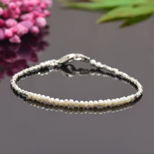 Puede incluir: Un delicado brazalete con una sola fila de pequeñas perlas blancas intercaladas con cuentas plateadas. El brazalete tiene un cierre plateado.