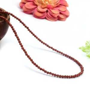 Puede incluir: Una larga hebra de cuentas de piedras preciosas marrones, ensartadas para formar un collar. Las cuentas son pequeñas y tienen una superficie rugosa y texturizada.