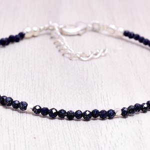 May include: A delicate bracelet featuring small, faceted, dark blue beads strung together. The bracelet has silver-colored accents and a matching clasp. This jewelry piece is designed for everyday wear.