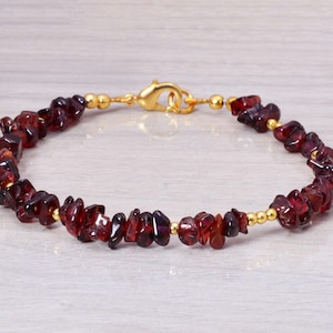 Op de afbeelding: Een gouden kettingarmband met kleine, onregelmatige rode edelsteen kralen.