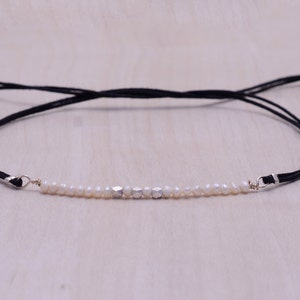 Puede incluir: Un brazalete delicado con un cordón negro y una fila de perlas blancas y cuentas plateadas.