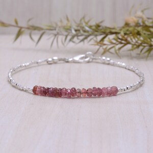May include: A delicate silver bracelet with a row of pink tourmaline gemstones. The bracelet is made with tiny silver beads and has a lobster clasp closure.