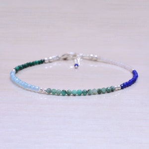 May include: A delicate bracelet with a gradient of blue, green, and white beads. The bracelet is made with small, round beads and has a silver clasp.