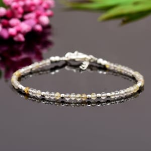 May include: A delicate silver bracelet with small, clear and golden beads. The bracelet is made of tiny, round beads that are strung together on a silver chain.