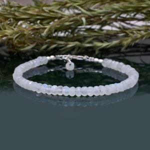 Op de afbeelding: Een delicate zilveren armband met een rij witte maansteen kralen. De armband ligt op een donkere achtergrond.