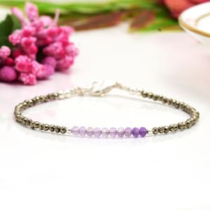Peut inclure: Un bracelet délicat avec une rangée de perles d'améthyste graduées dans des tons de violet et une rangée de perles de pyrite dorée. Le bracelet est fait en argent sterling.