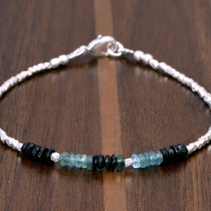 Puede incluir: Un brazalete de plata con cierre de broche, que presenta cuentas de piedras preciosas negras y azules alternadas.