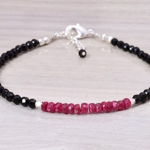 Könnte beinhalten: Ein schwarzes und rotes Perlenarmband mit einem silbernen Verschluss. Das Armband besteht aus kleinen, facettierten schwarzen Perlen und einer Reihe roter Perlen in der Mitte.