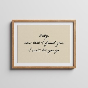 May include: A framed wall art print featuring a light beige background with black cursive text that reads: Baby, now that I found you, I can't let you go. The print is enclosed in a simple, light-toned wooden frame with a clean, rectangular border.