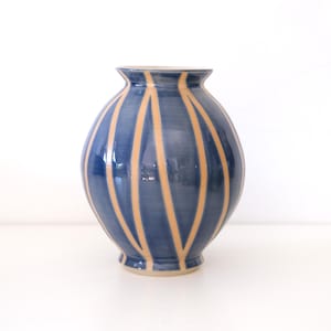 May include: A blue ceramic vase with a rounded body and a narrow opening. The vase is decorated with vertical stripes of a lighter color.