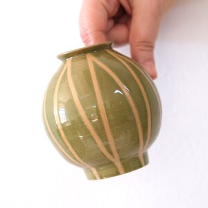 May include: A green ceramic vase with a rounded shape and a striped pattern in a lighter shade of brown.