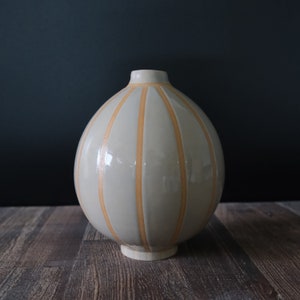 May include: A light gray ceramic vase with vertical orange stripes. The vase has a rounded, bulbous shape.